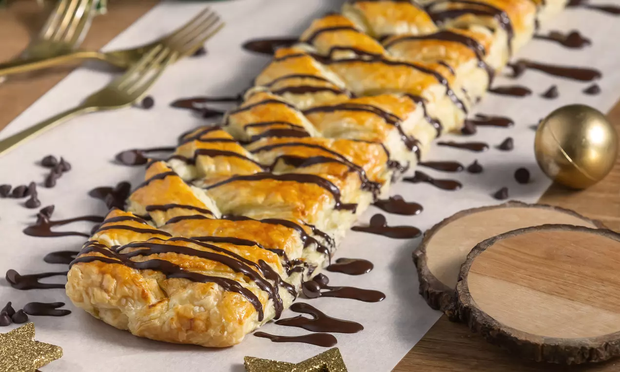 Aranybarna leveles tészta rombuszokra vágva, a tetején lágyan csurgatott étcsokoládé, rusztikus fa tálalón körülötte csillag alakú dekorációval